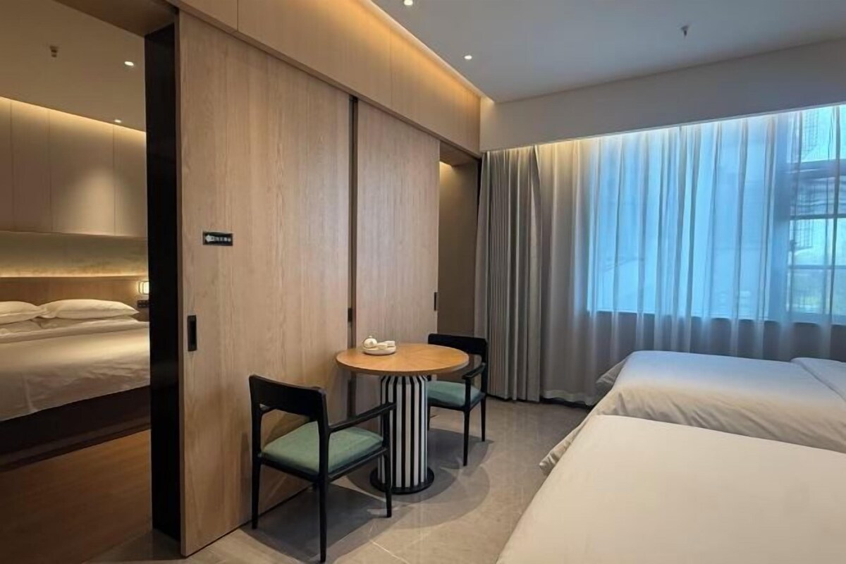 Ein Hotelzimmer mit einem Bett, einem Schreibtisch mit zwei Stühlen, einem kleinen Tisch und einem Fenster mit Vorhängen.