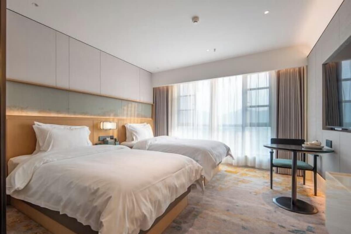 Habitación de hotel con dos camas, una mesita y vista al exterior.