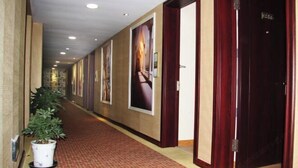 Een hotelgang met een rood tapijt, houten deuren en ingelijste foto's aan de muur.