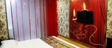 Habitación de hotel con cama, cortinas rojas, televisor montado en la pared y un panel decorativo.
