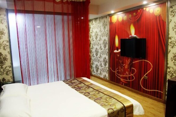 Une chambre d’hôtel avec un lit, des rideaux rouges, un téléviseur fixé au mur et un panneau décoratif.