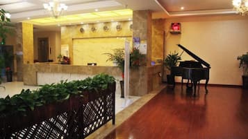 Un vestíbulo de hotel con una recepción, un piano de cola y una araña.