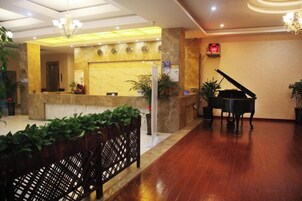 Um saguão de hotel com balcão de recepção, um piano de cauda e um candelabro.