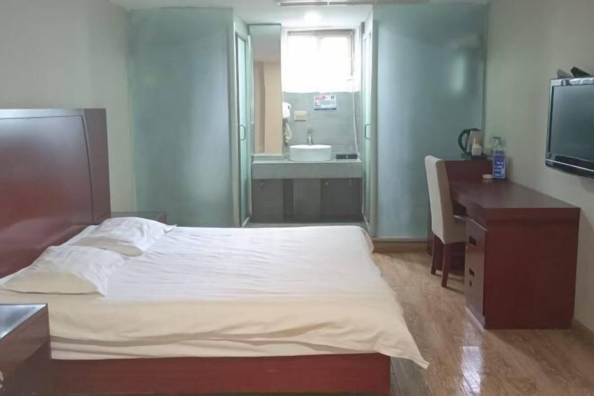 Une chambre d’hôtel avec un lit, un bureau, une télévision et une salle de bain visible à travers une porte ouverte.
