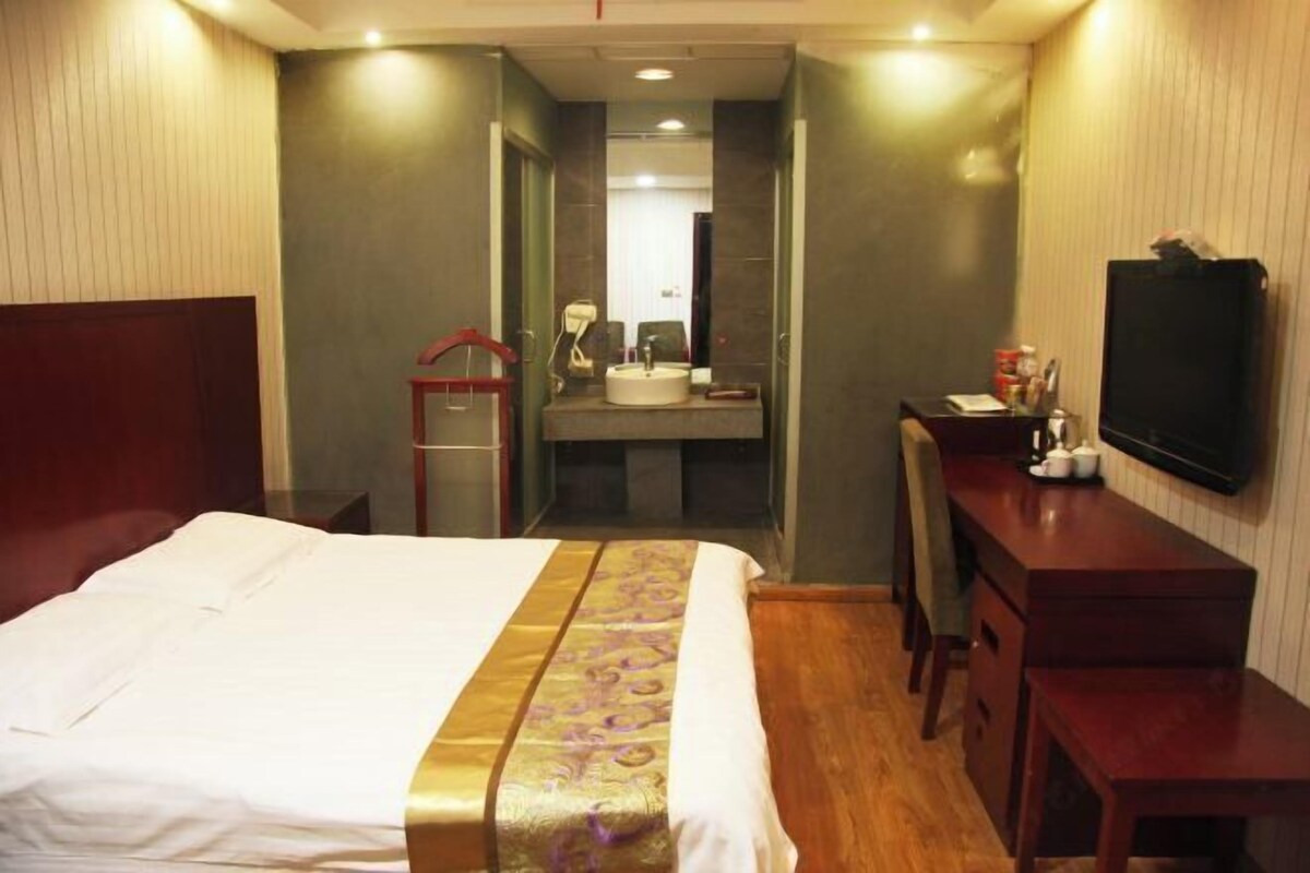 Une chambre d’hôtel avec un lit, un bureau, une télévision, un miroir et une salle de bain visible à travers une porte ouverte.