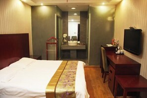 Une chambre d’hôtel avec un lit, un bureau, une télévision, un miroir et une salle de bain visible à travers une porte ouverte.