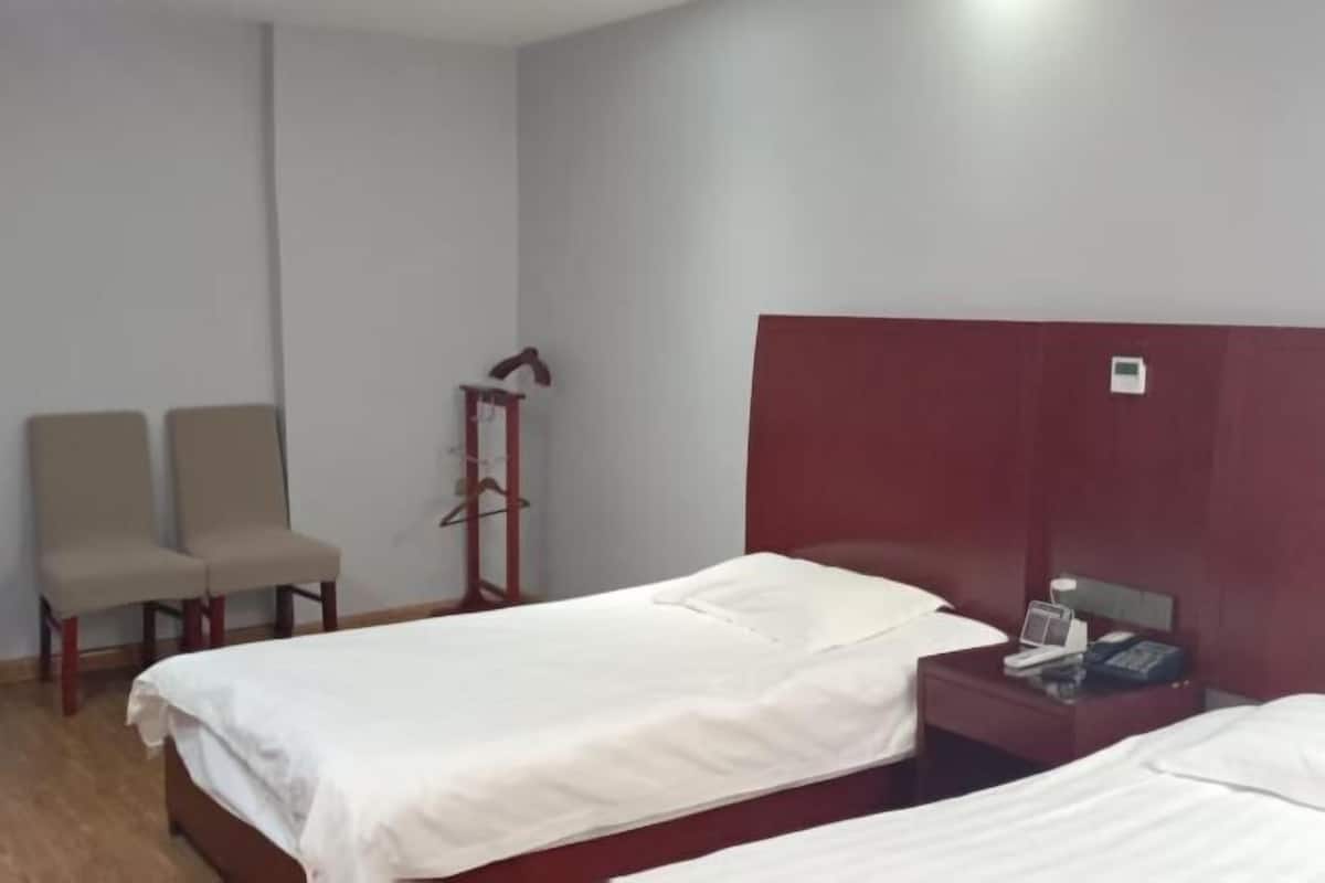 Une chambre d’hôtel avec deux lits simples, un petit bureau avec un téléphone et deux chaises.