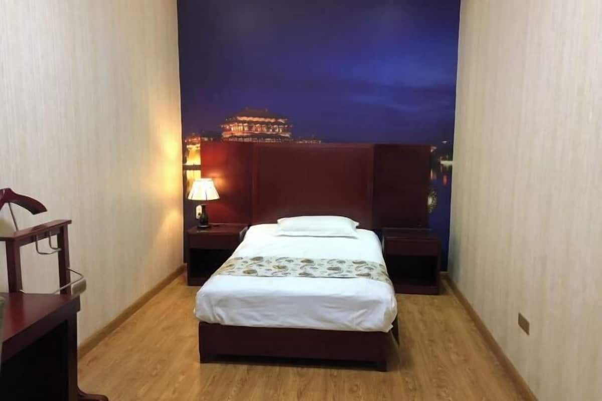 Une chambre d’hôtel avec un lit, une table de chevet avec une lampe et une vue sur un immeuble la nuit.