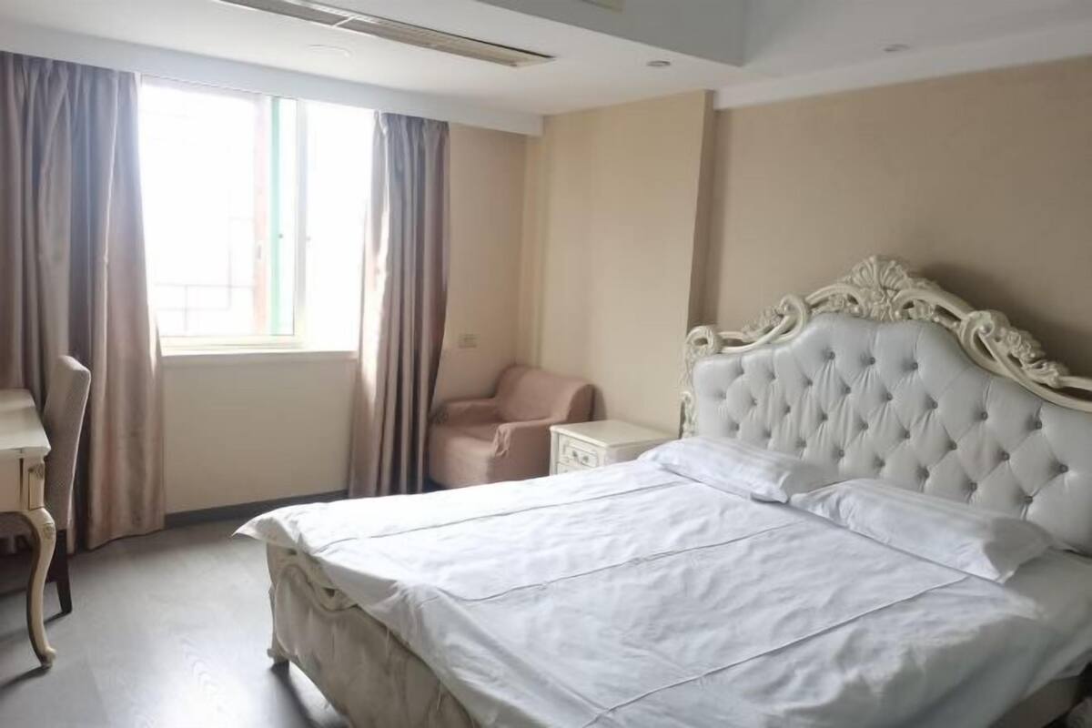 Une chambre d’hôtel avec un grand lit, une table de chevet, une chaise et une fenêtre avec des rideaux.
