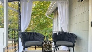 A covered porch with two black wicker chairs, a decorative metal lantern, and a tropical leaf-patterned rug.