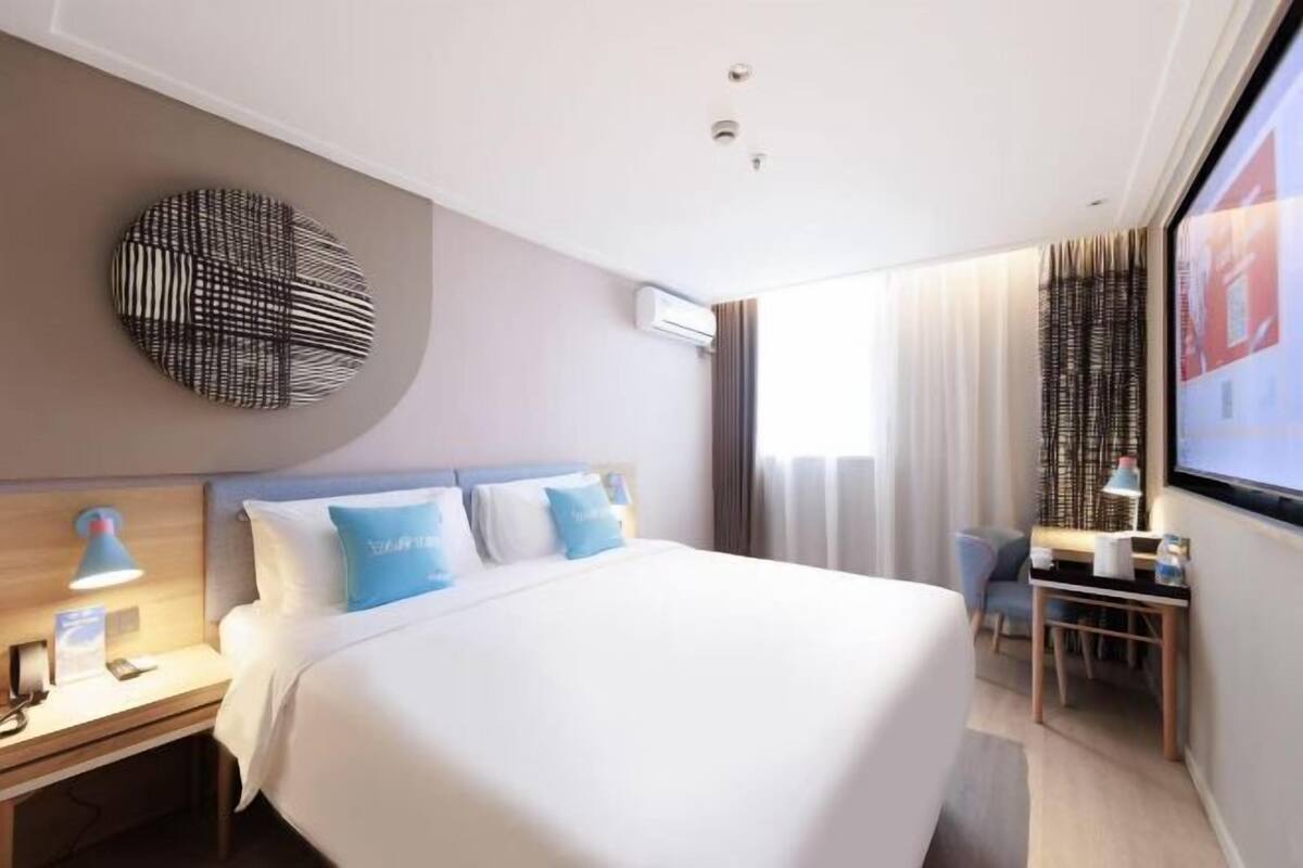 A modern hotel room with a large bed, a desk, and a TV.