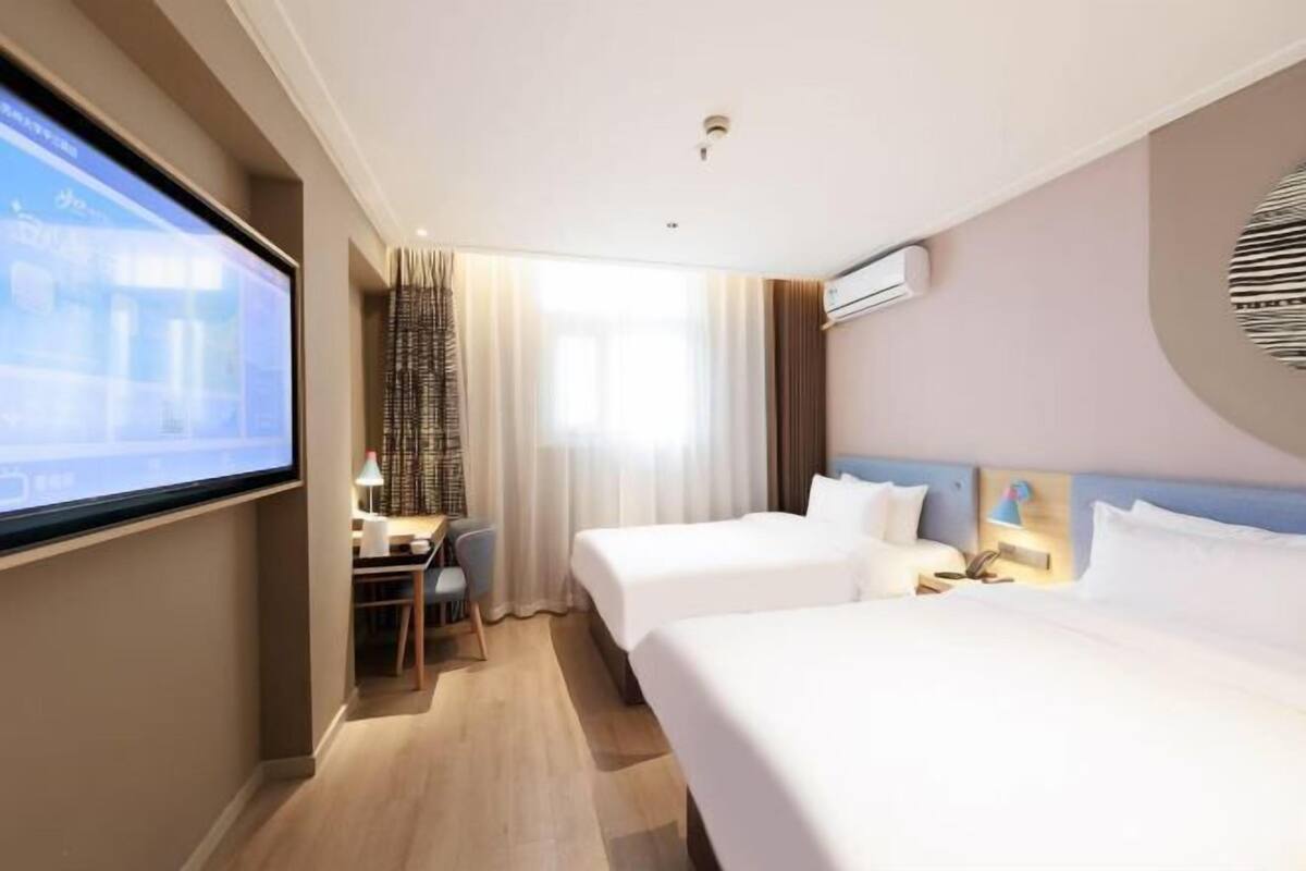 A hotel room with two beds, a desk, a chair, a TV screen, and a window with curtains.
