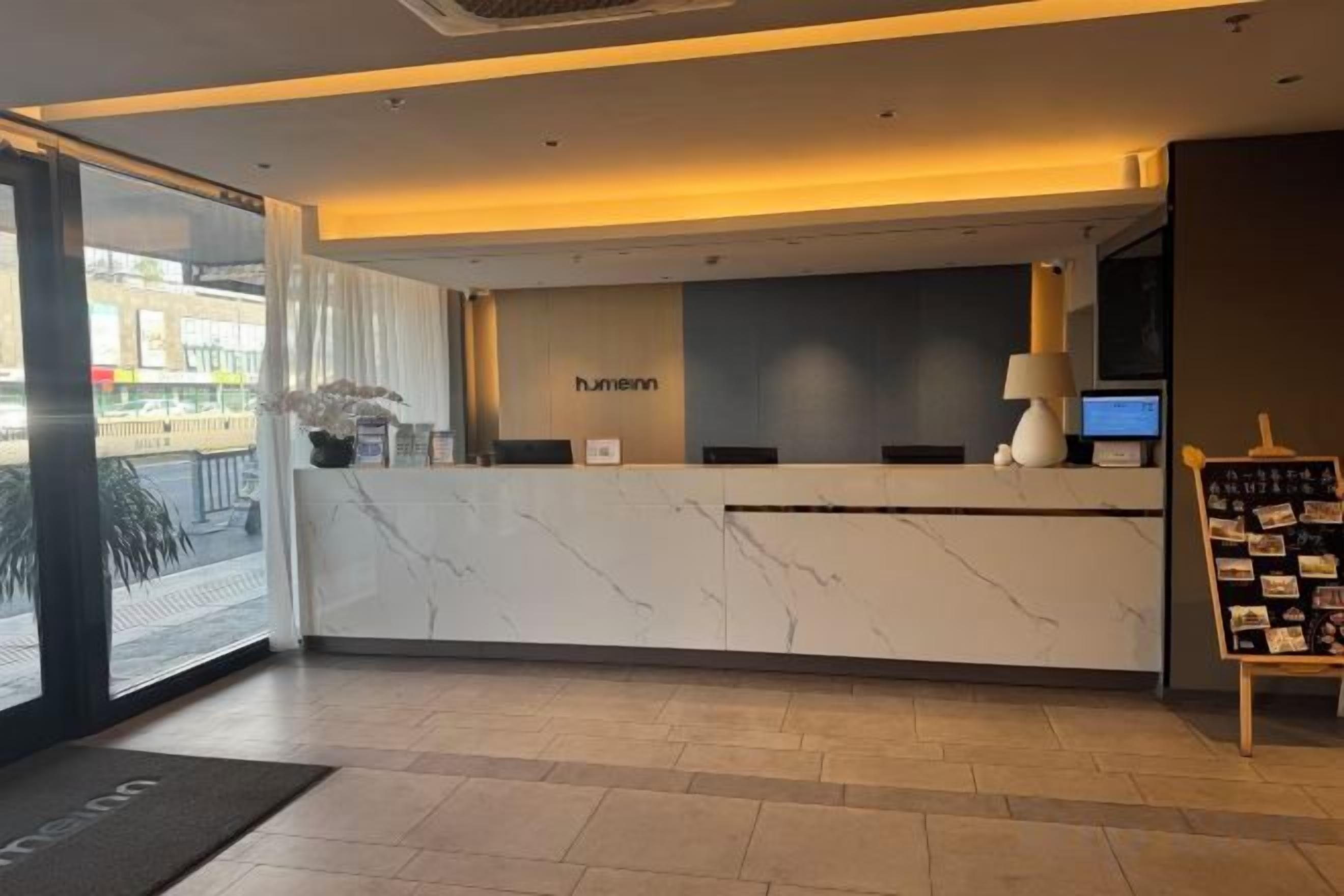Balcão de recepção de hotel com bancada de mármore, uma tela digital e uma placa com a inscrição 'hummel'.