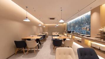 A modern dining area with multiple tables and chairs, a counter with a display, and pendant lighting.