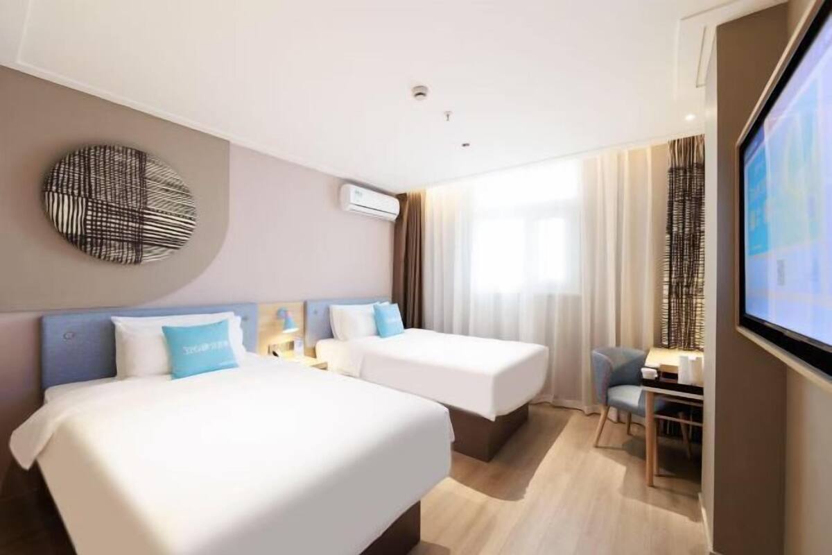 A hotel room with two beds, a desk, and a TV.