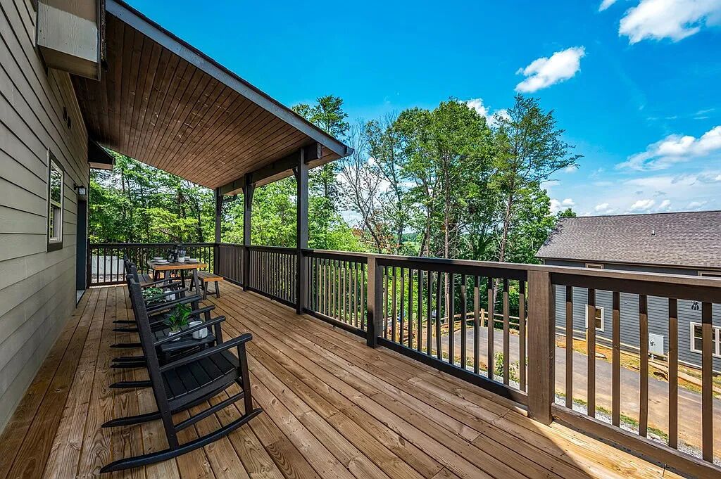 Une terrasse en bois avec des meubles d’extérieur, un espace abrité et une vue sur les arbres et une route.