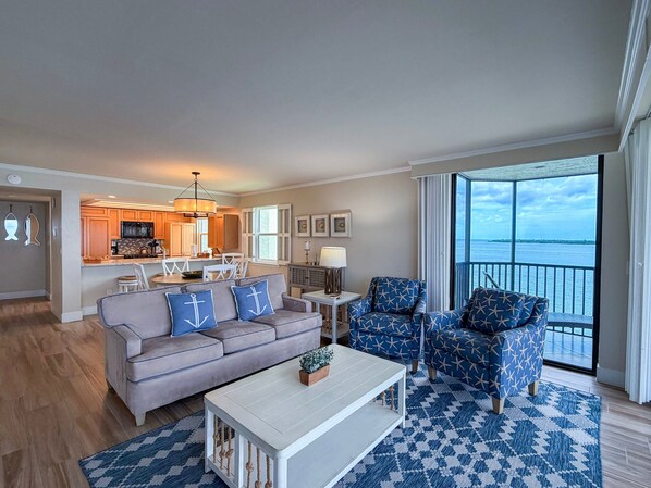 A modern living room with a sofa, armchairs, a coffee table, and a view of the sea through large windows.