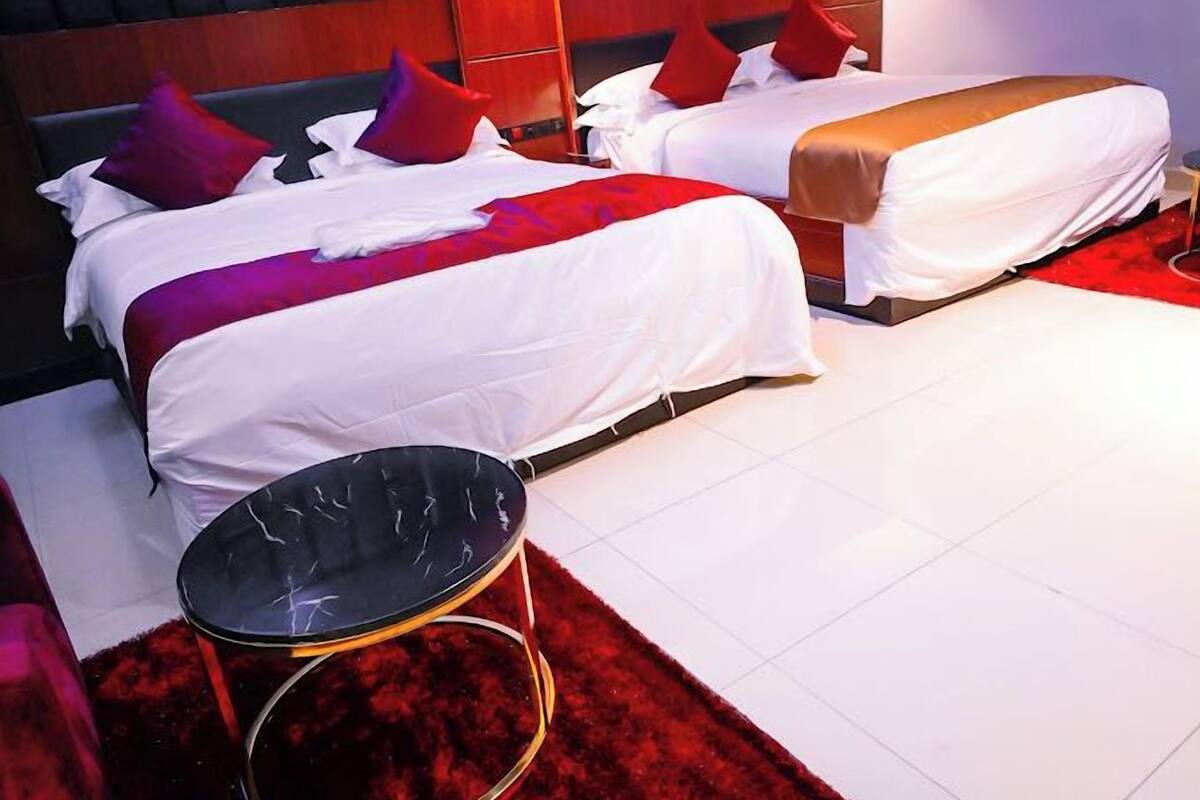 Une chambre d’hôtel avec deux lits, une moquette rouge et une table ronde noire.