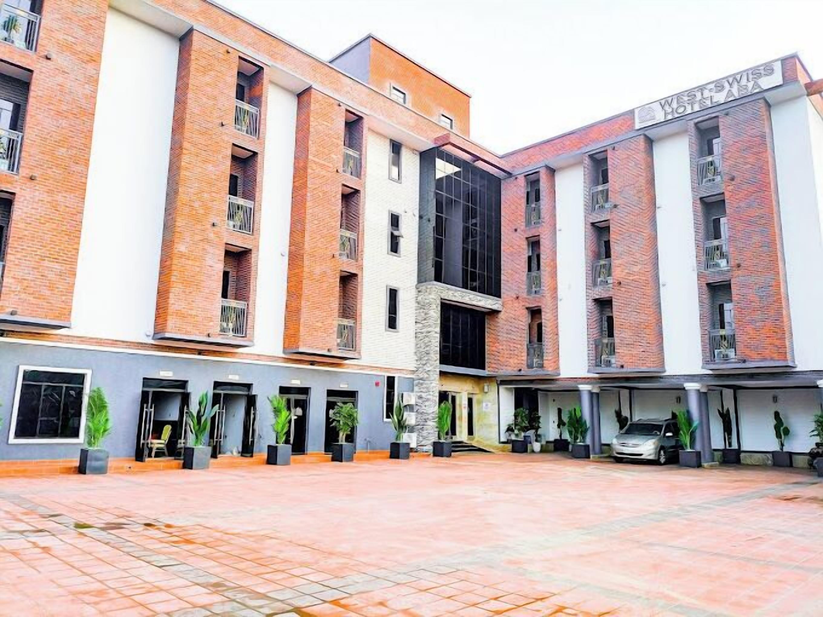 A multi-story hotel with a brick facade, multiple balconies, and a central courtyard with potted plants.