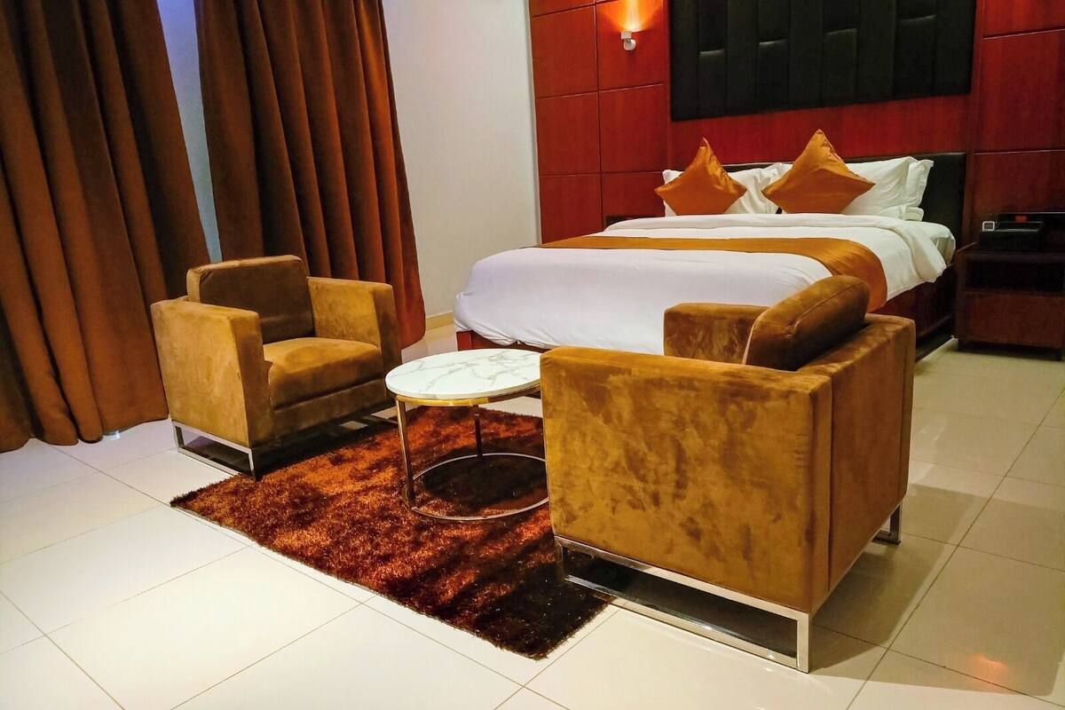Une chambre d’hôtel avec un lit, deux fauteuils, une petite table ronde et un mur d’accent rouge.