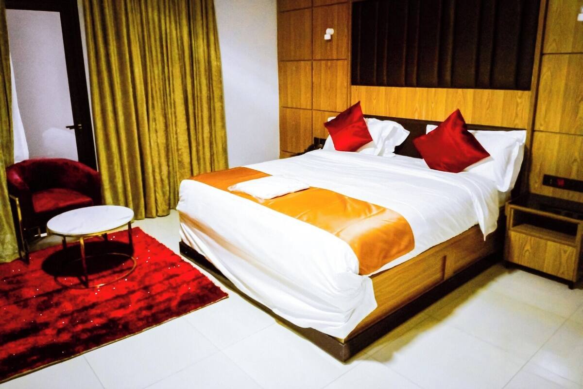 Une chambre d’hôtel avec un grand lit, un fauteuil rouge, une petite table ronde et un tapis rouge.