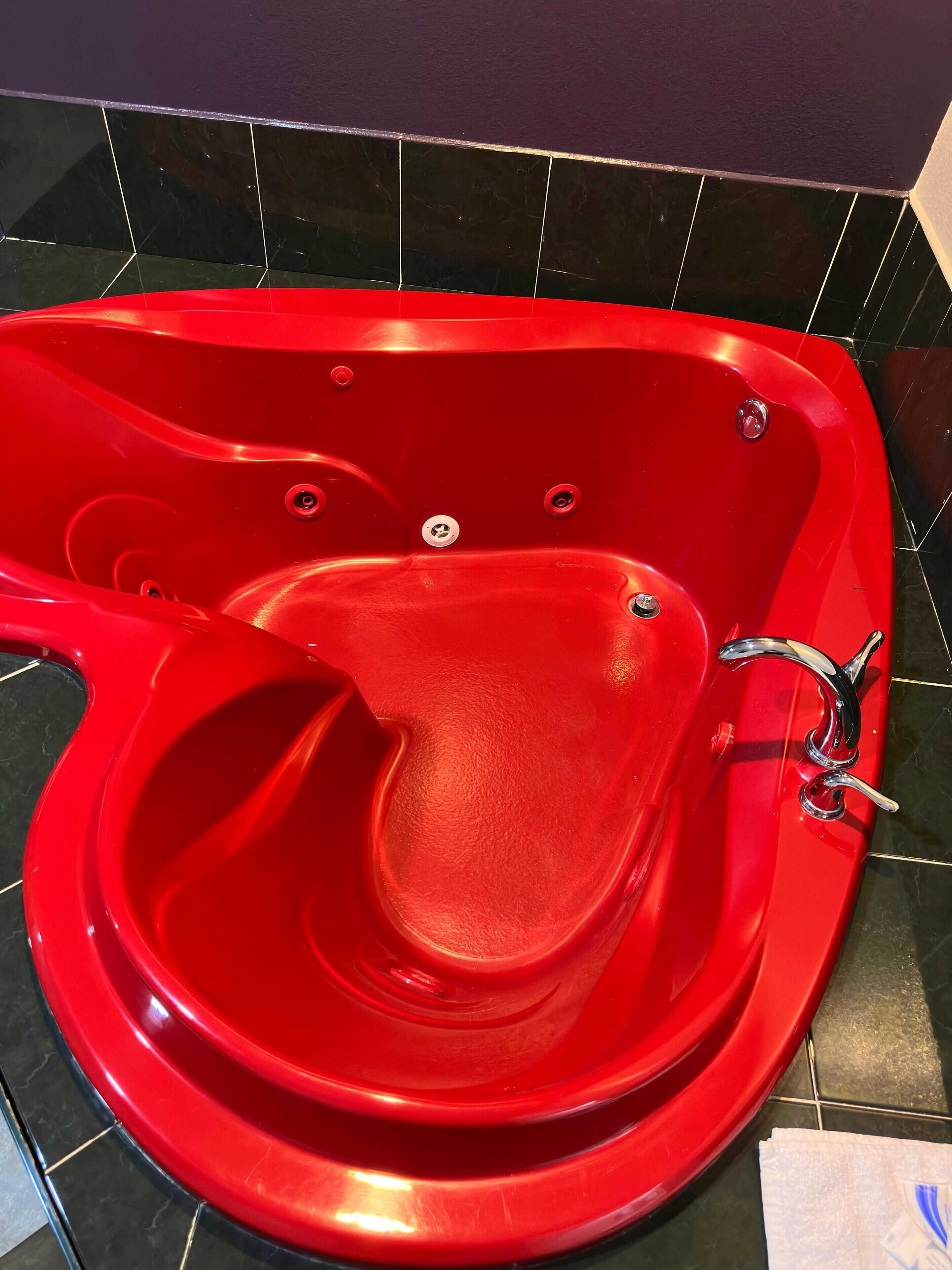 A red jacuzzi tub with multiple jets, set against a dark tiled wall.