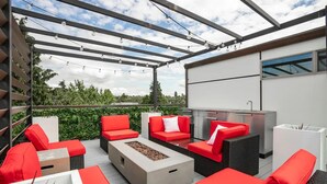 Une terrasse extérieure avec des meubles rouges et blancs, un foyer intégré et une pergola décorée de guirlandes lumineuses.
