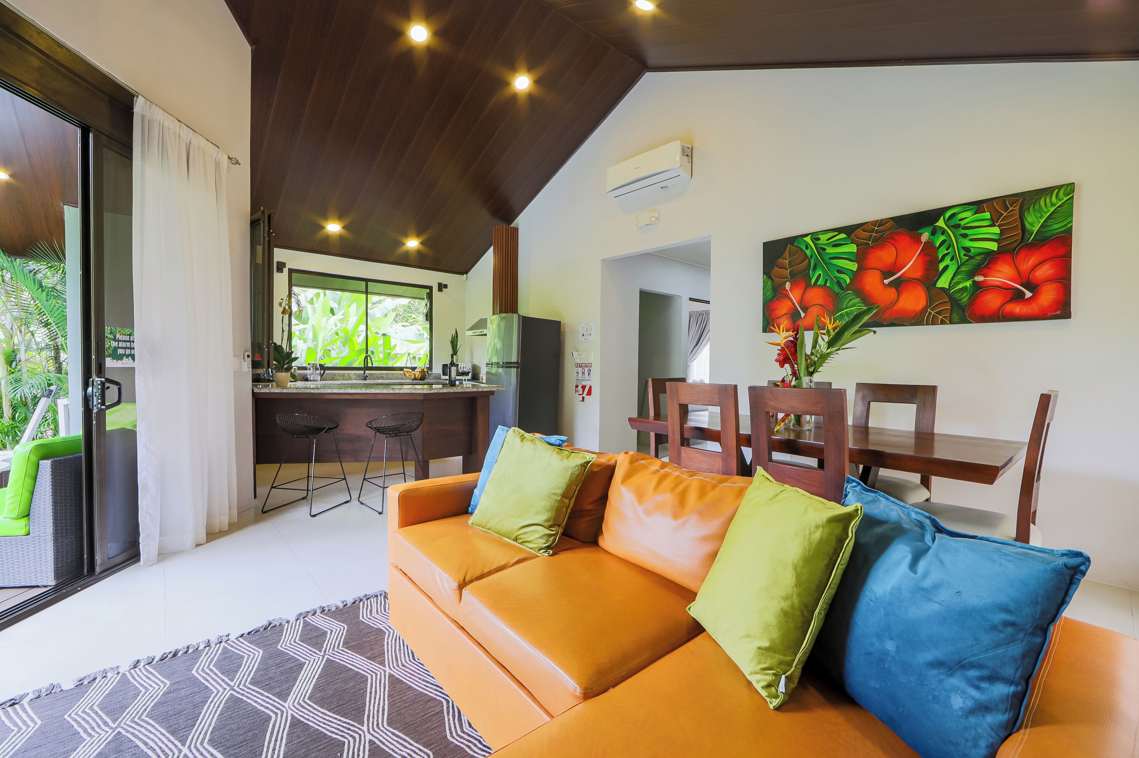 Una sala moderna con sofá de cuero, un comedor con muebles de madera y una cocina al fondo.