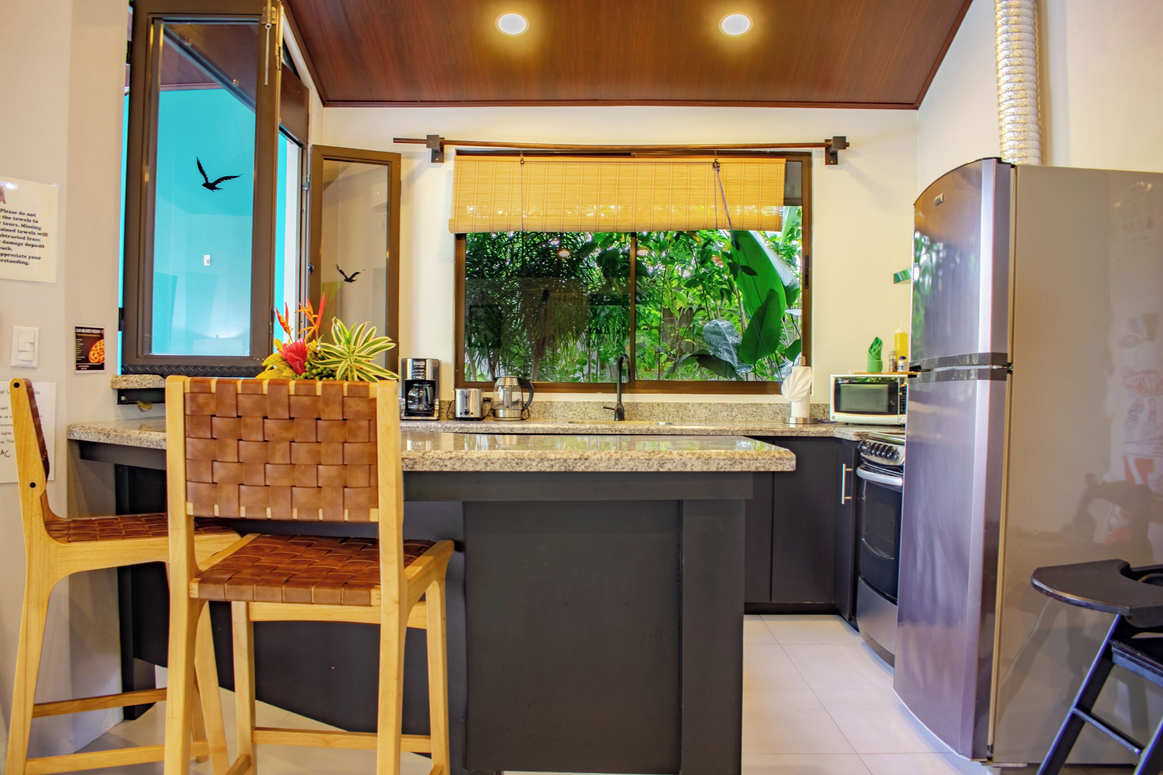 A modern kitchen with a central island, stainless steel appliances, and a view of greenery outside.