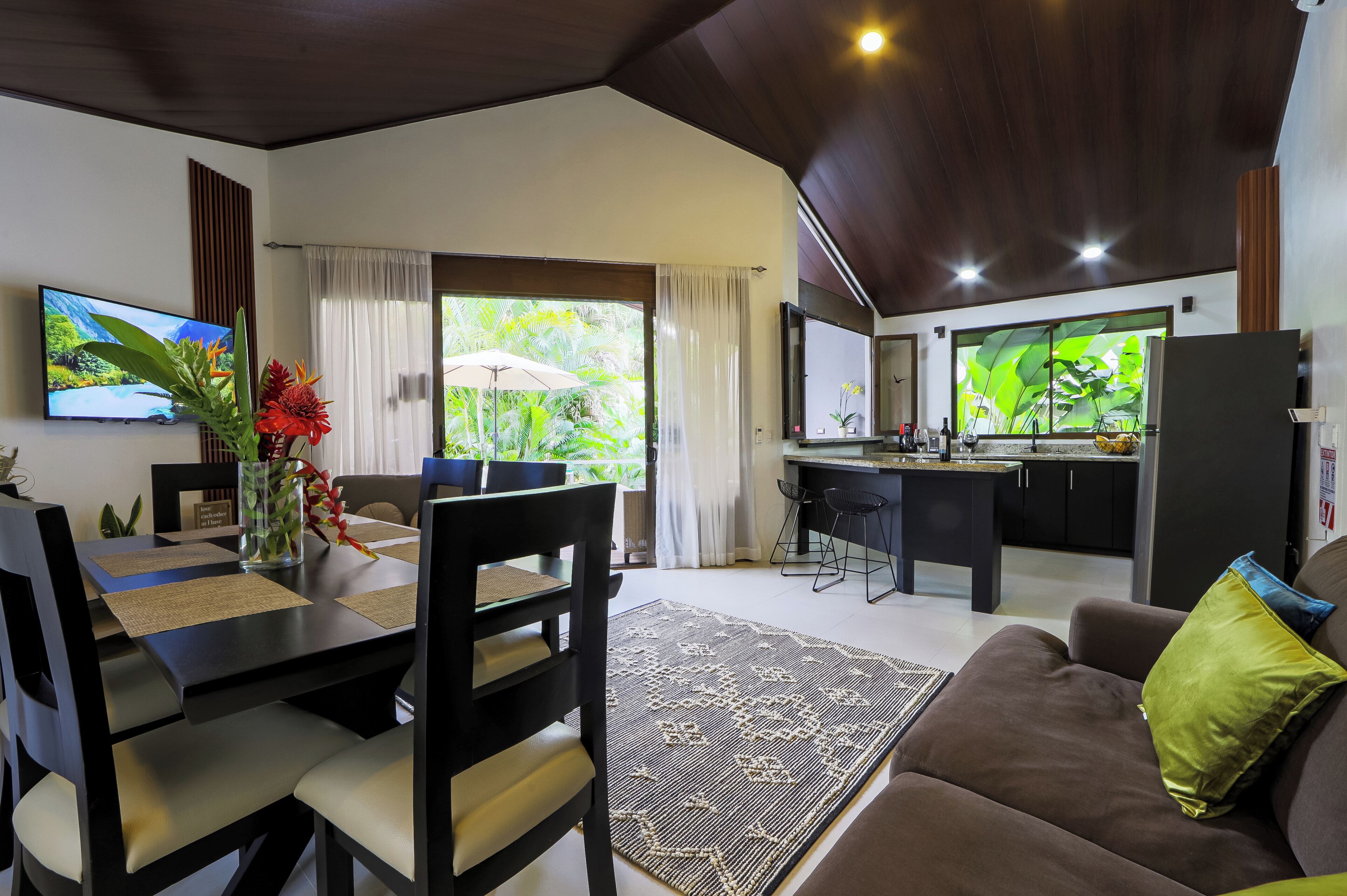 A modern living room with a dining area, a kitchen, and a large window with curtains.