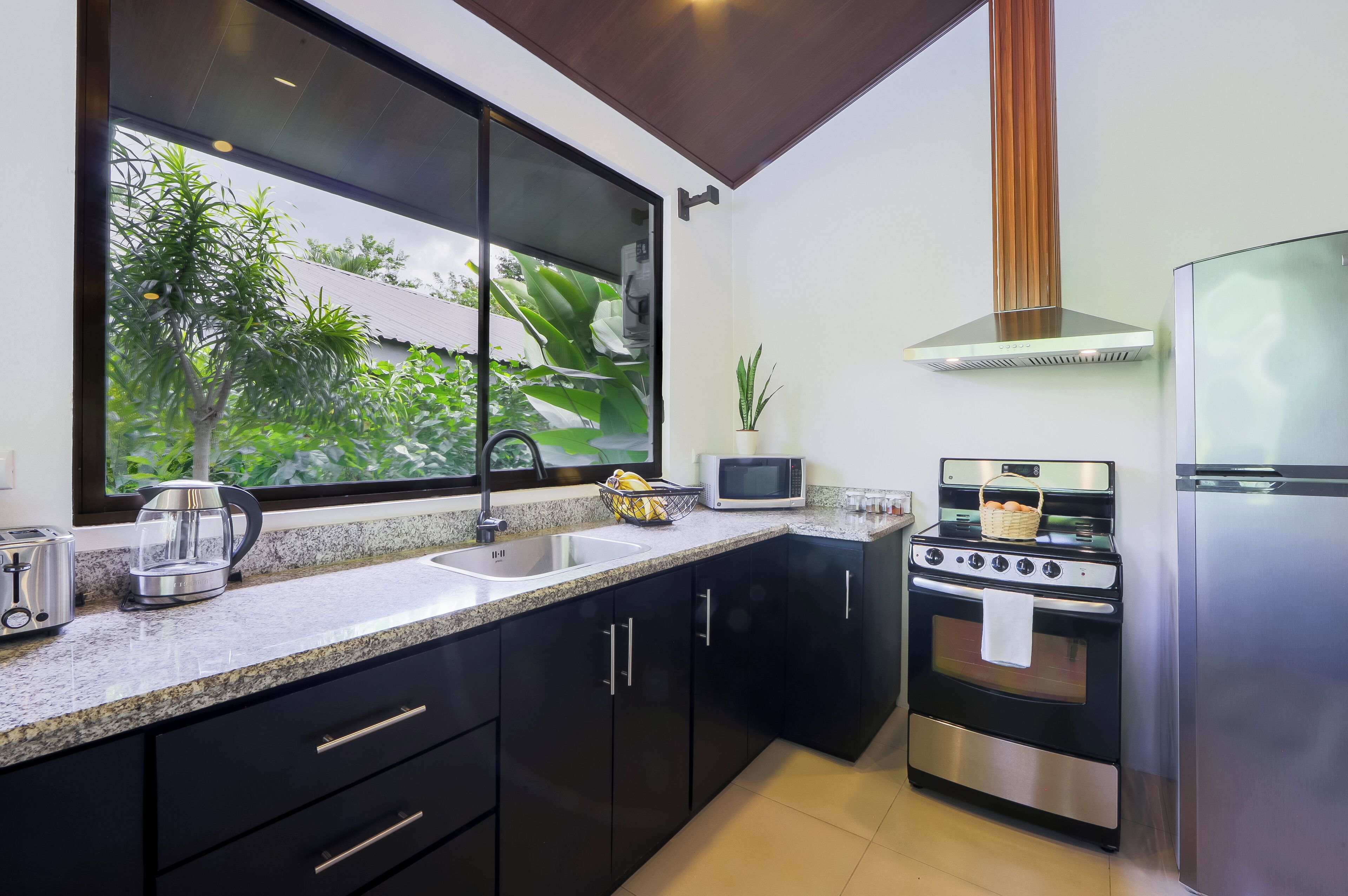 Una cocina moderna con un ventanal grande, electrodomésticos de acero inoxidable y armarios negros.