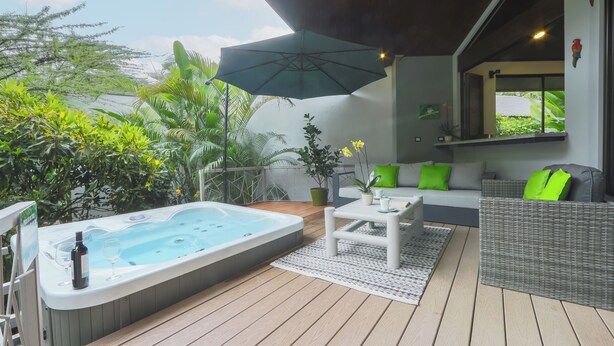 A hot tub, outdoor seating, and lush greenery on a wooden deck. - Bukala Village Lodge (Peñas Blancas)