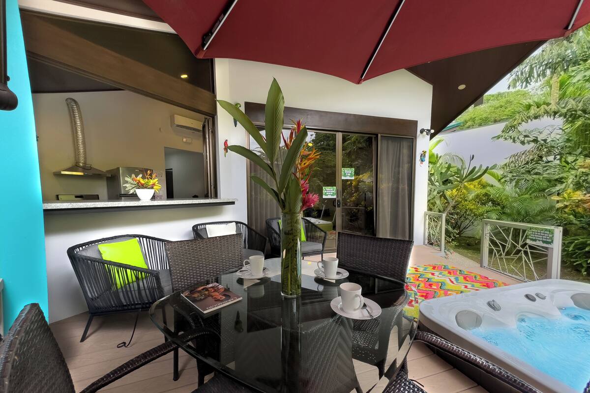 A glass-top table with chairs, a hot tub, and a patio area with a view of the garden.