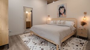 Une chambre à coucher avec un grand lit, une tête de lit en bois, un tableau accroché au mur et une table de chevet avec une lampe.