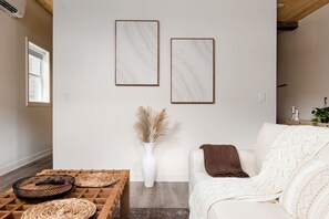 A modern living room with a white sofa, a wooden coffee table, and two framed artworks on the wall. - Pine Beam Sloth Apartment next to Blue Line (Chicago)