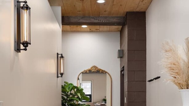 Un couloir avec un plancher en bois, un miroir, une plante en pot et un meuble en bois doté de tiroirs.