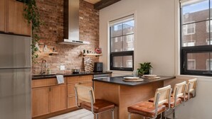 Une cuisine moderne avec un mur en briques, des armoires en bois, un réfrigérateur en acier inoxydable et un coin bar avec des tabourets.