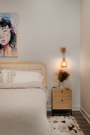 A bedroom with a bed, bedside table, lamp, and a painting on the wall. - Pine Beam Sloth Apartment next to Blue Line (Chicago)