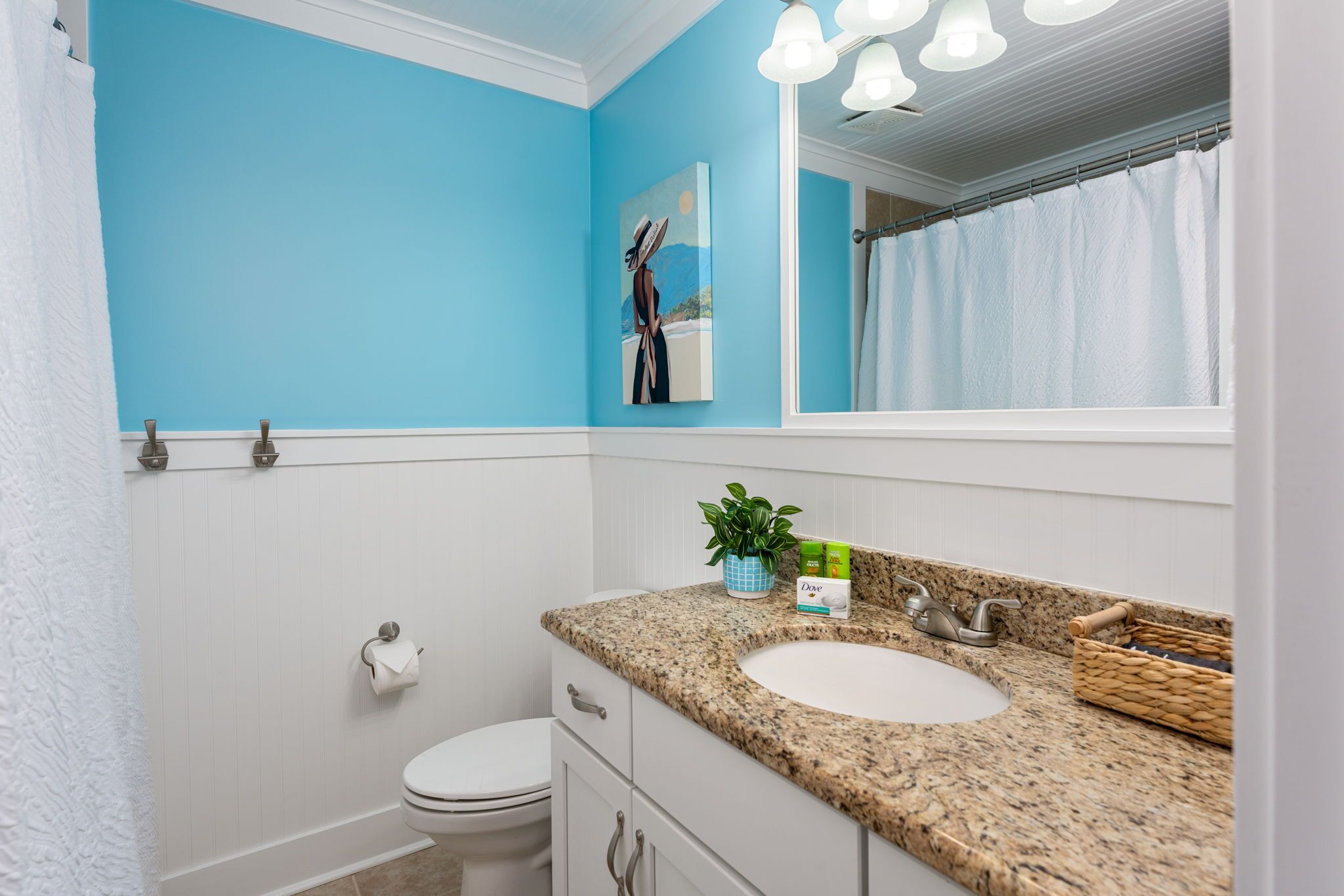A bathroom with a blue wall, a white toilet, a granite sink, and a mirror above the sink.
