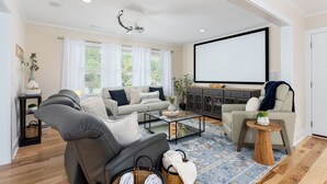 A living room with a sofa, armchairs, a coffee table, a TV, and a projector. - Luxurious & Comfy Haven: Prime Location ~ Pool ~ Hot Tub ~ Fire Pit ~ Gym ~ Pkg! (Wilmington)