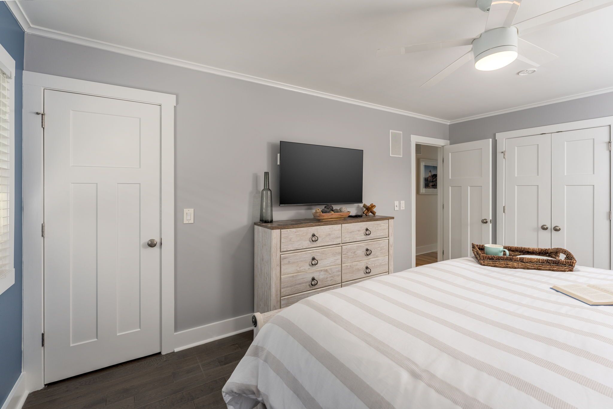 Un dormitorio con cama, cómoda, televisor y ventilador de techo.