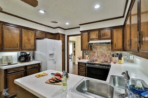 Una cocina con armarios de madera, un refrigerador, una cafetera y un salpicadero de azulejos.