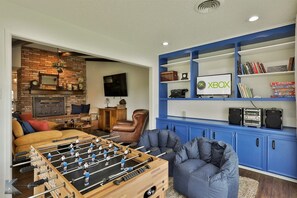 Ein Wohnzimmer mit einem Kicker, einer blauen Unterhaltungsanlage mit einer Xbox und einem Kamin aus Backstein.