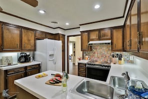 A kitchen with wooden cabinets, a refrigerator, a coffee maker, and a tiled backsplash. - Maxine's Place- A Wonderful Family Legacy (Abilene)