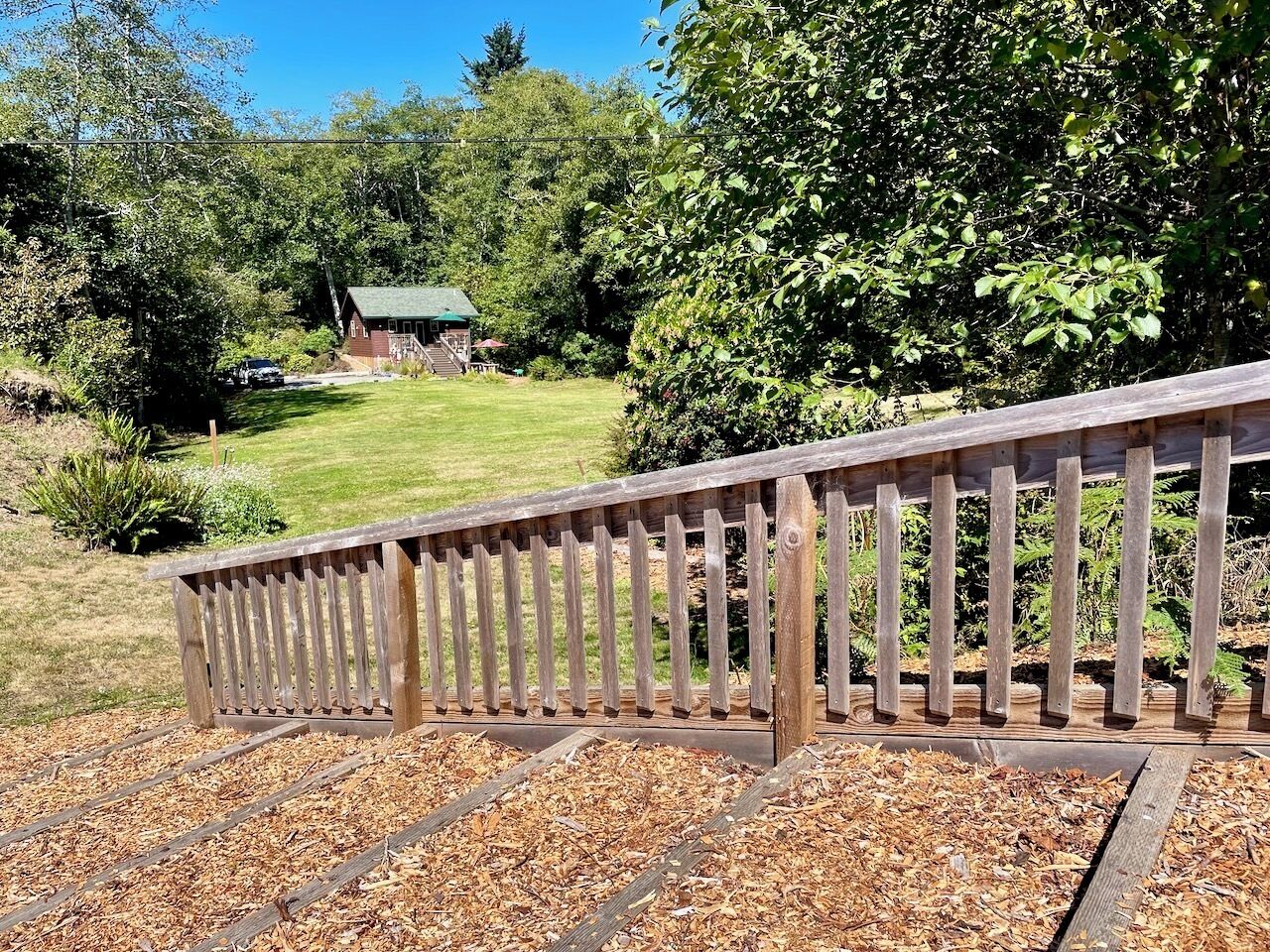 A wooden deck with a metal railing, surrounded by mulch and trees.