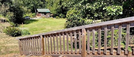 A wooden deck with a metal railing, surrounded by mulch and trees.