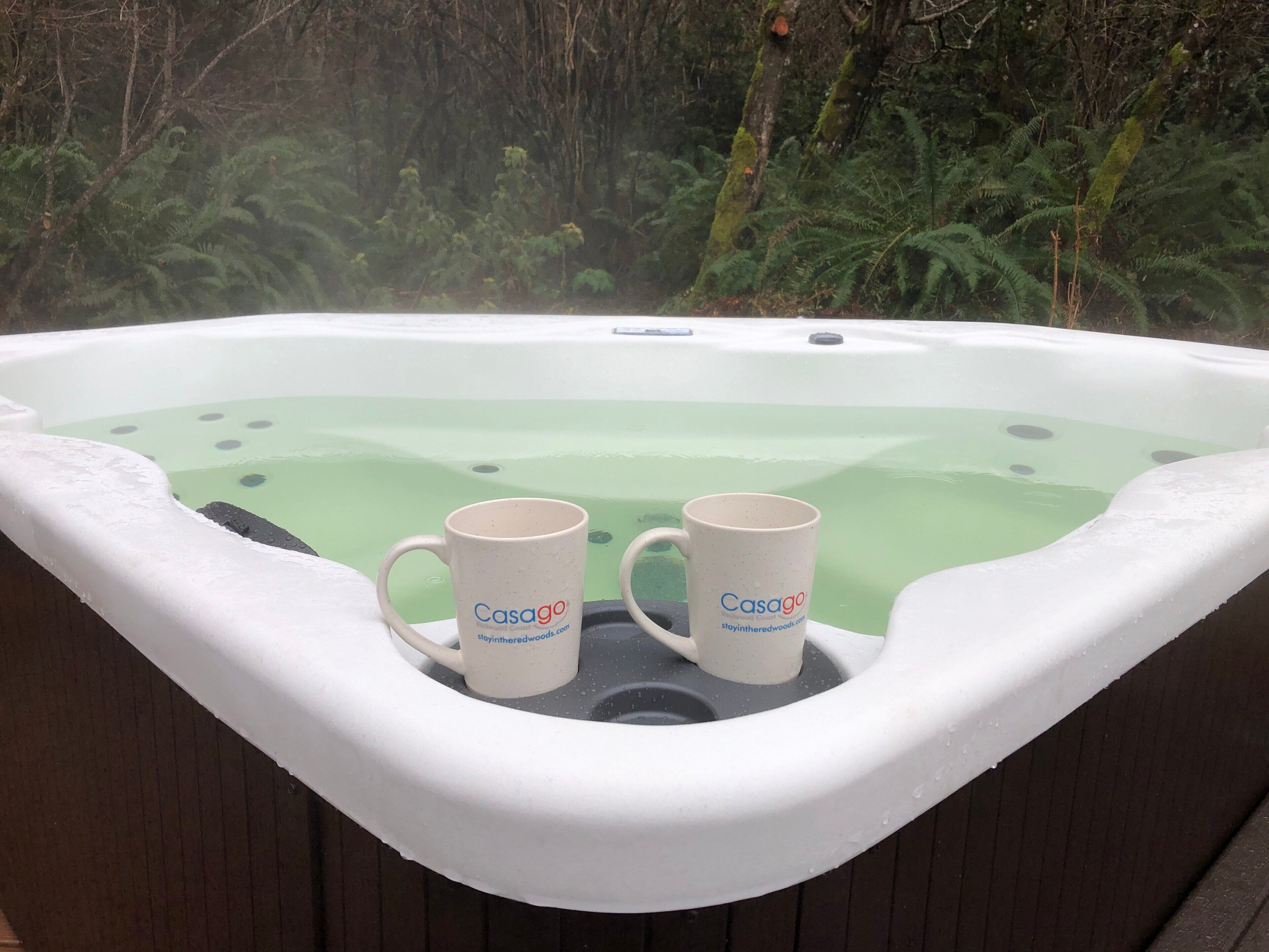 Un bain à remous avec deux tasses portant l’inscription « Casago » et un paysage boisé en arrière-plan.