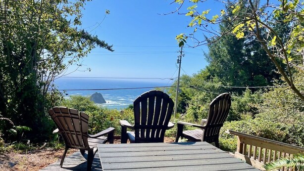 Une terrasse en bois avec des fauteuils Adirondack et une table, offrant une vue panoramique sur l’océan.