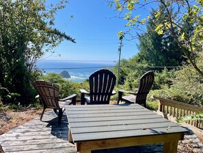 Une terrasse en bois avec des fauteuils Adirondack et une table, offrant une vue panoramique sur l’océan.
