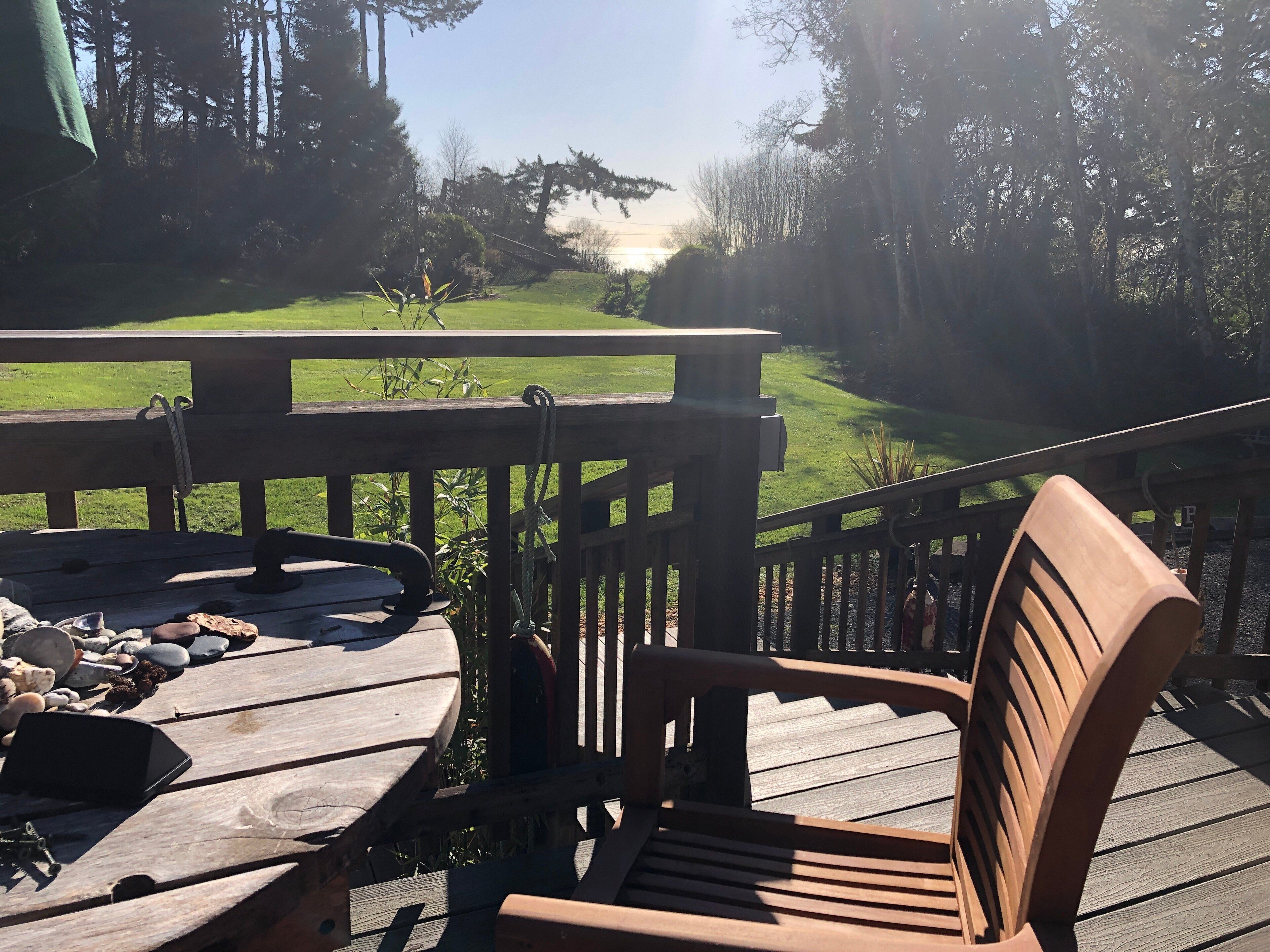 Une terrasse en bois avec une table et des chaises, donnant sur un espace verdoyant bordé d’arbres.
